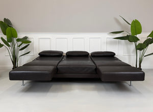 Gebrauchtes braunes Ledersofa Brühl Modell Moule 3 Sitzer vor einer modernen Wand.