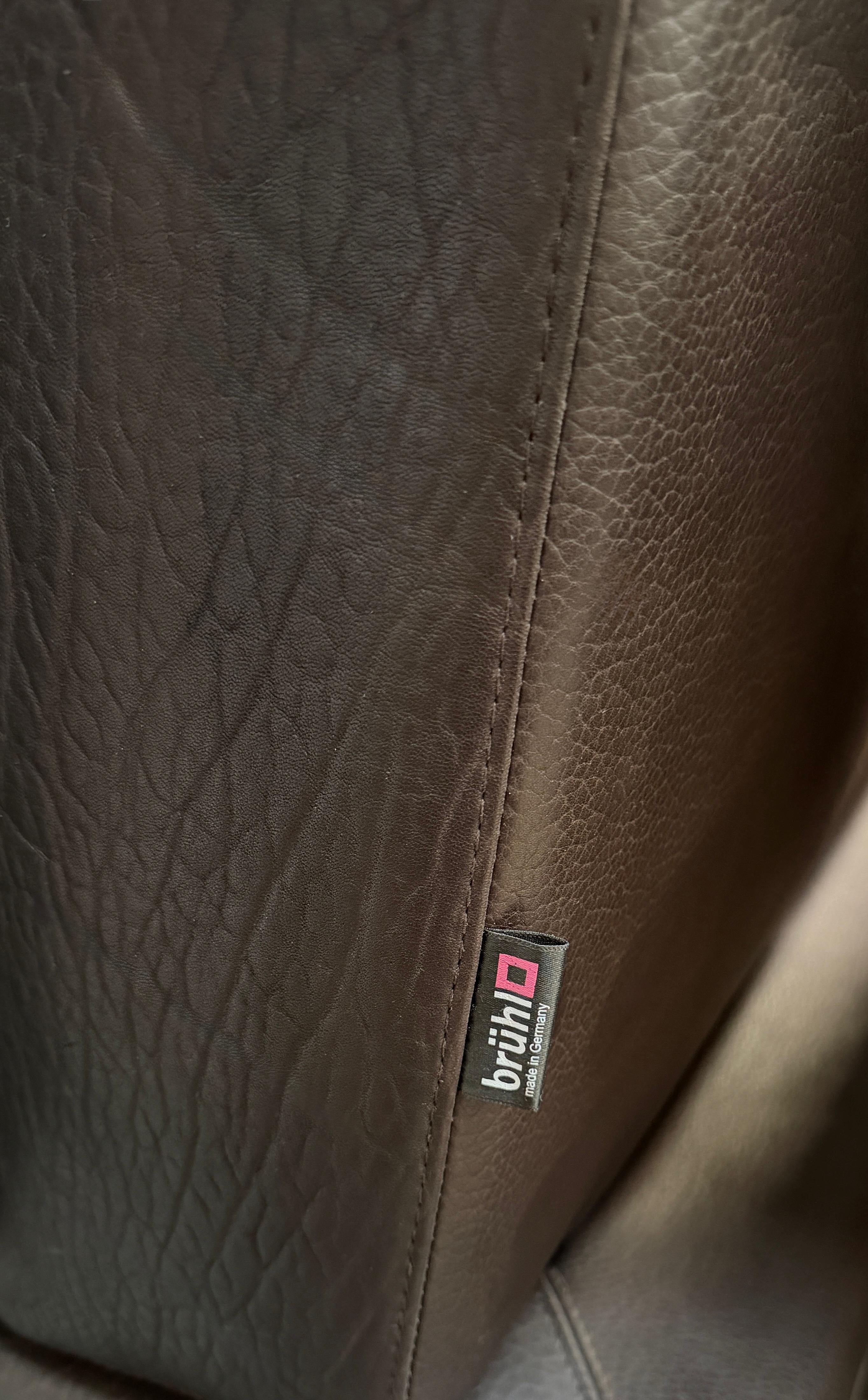 Gebrauchtes braunes Ledersofa Brühl Modell Moule 3 Sitzer vor einer modernen Wand.