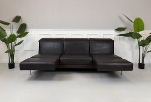 Gebrauchtes braunes Ledersofa Brühl Modell Moule 3 Sitzer vor einer modernen Wand.