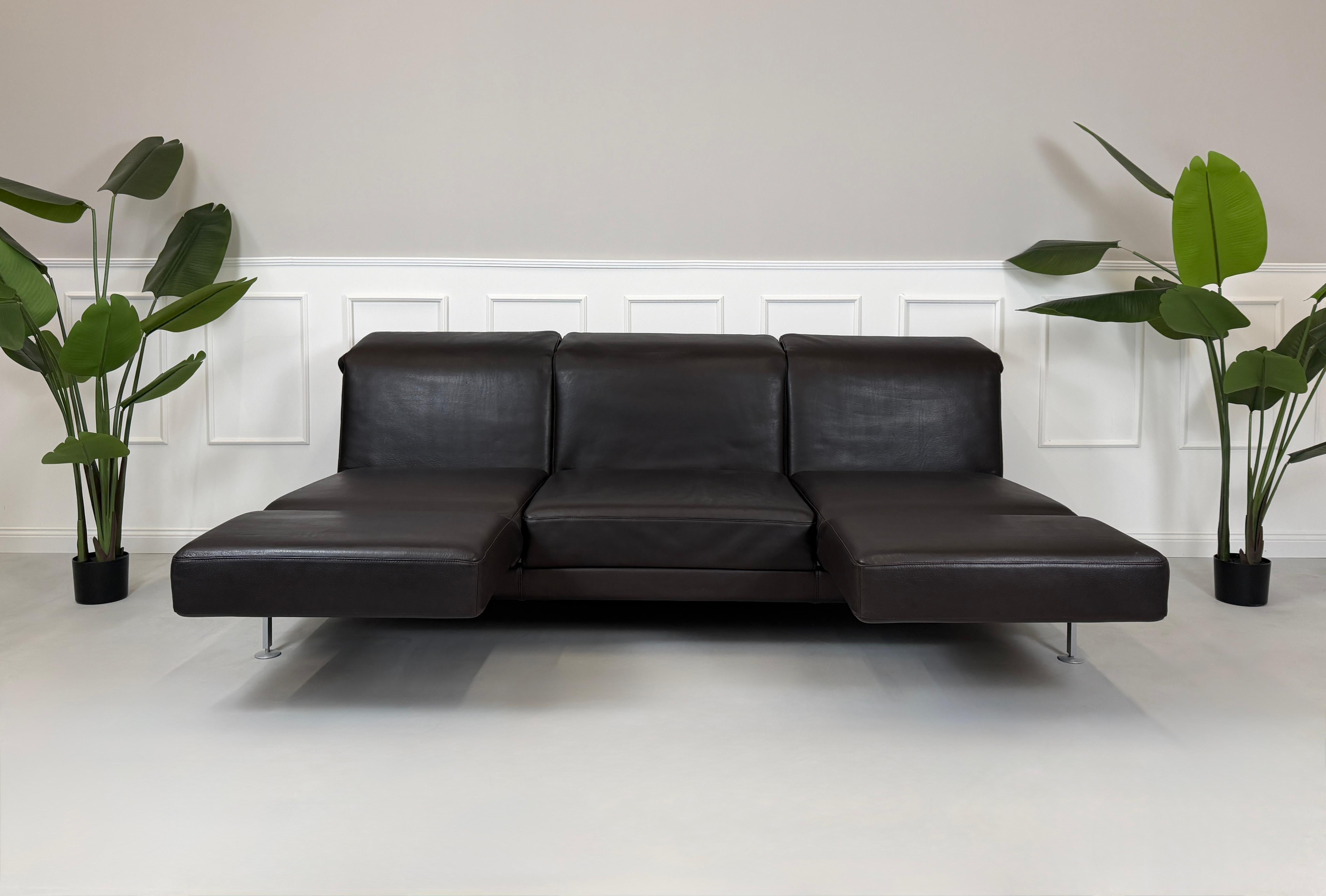 Gebrauchtes braunes Ledersofa Brühl Modell Moule 3 Sitzer vor einer modernen Wand.