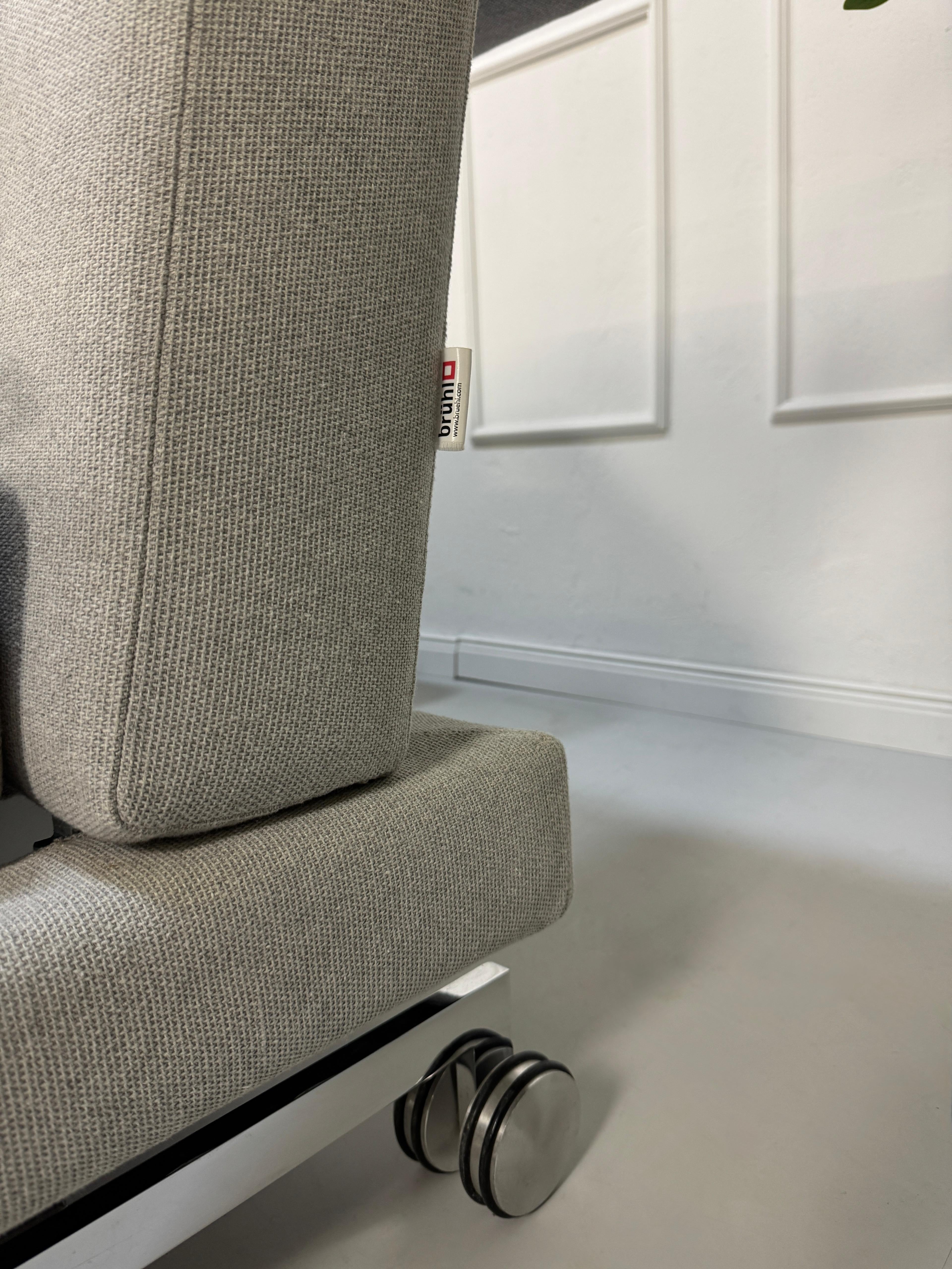 Gebrauchtes graues Brühl Moule Designer Stoff Sofa vor einer Wand, stilvoll und modern eingerichtet.