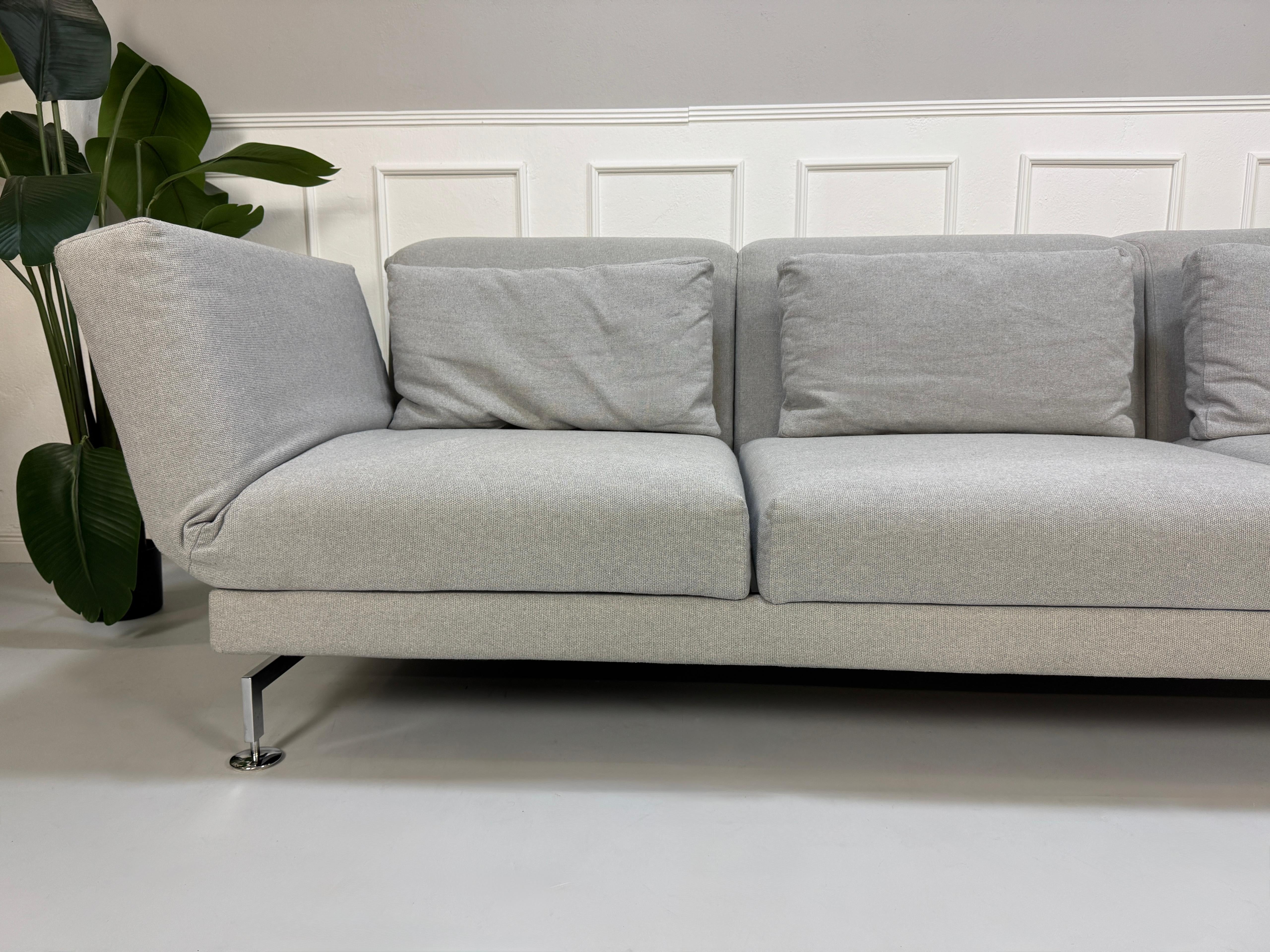 Gebrauchtes graues Brühl Moule Designer Stoff Sofa vor einer Wand, stilvoll und modern eingerichtet.