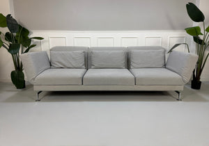 Gebrauchtes graues Brühl Moule Designer Stoff Sofa vor einer Wand, stilvoll und modern eingerichtet.
