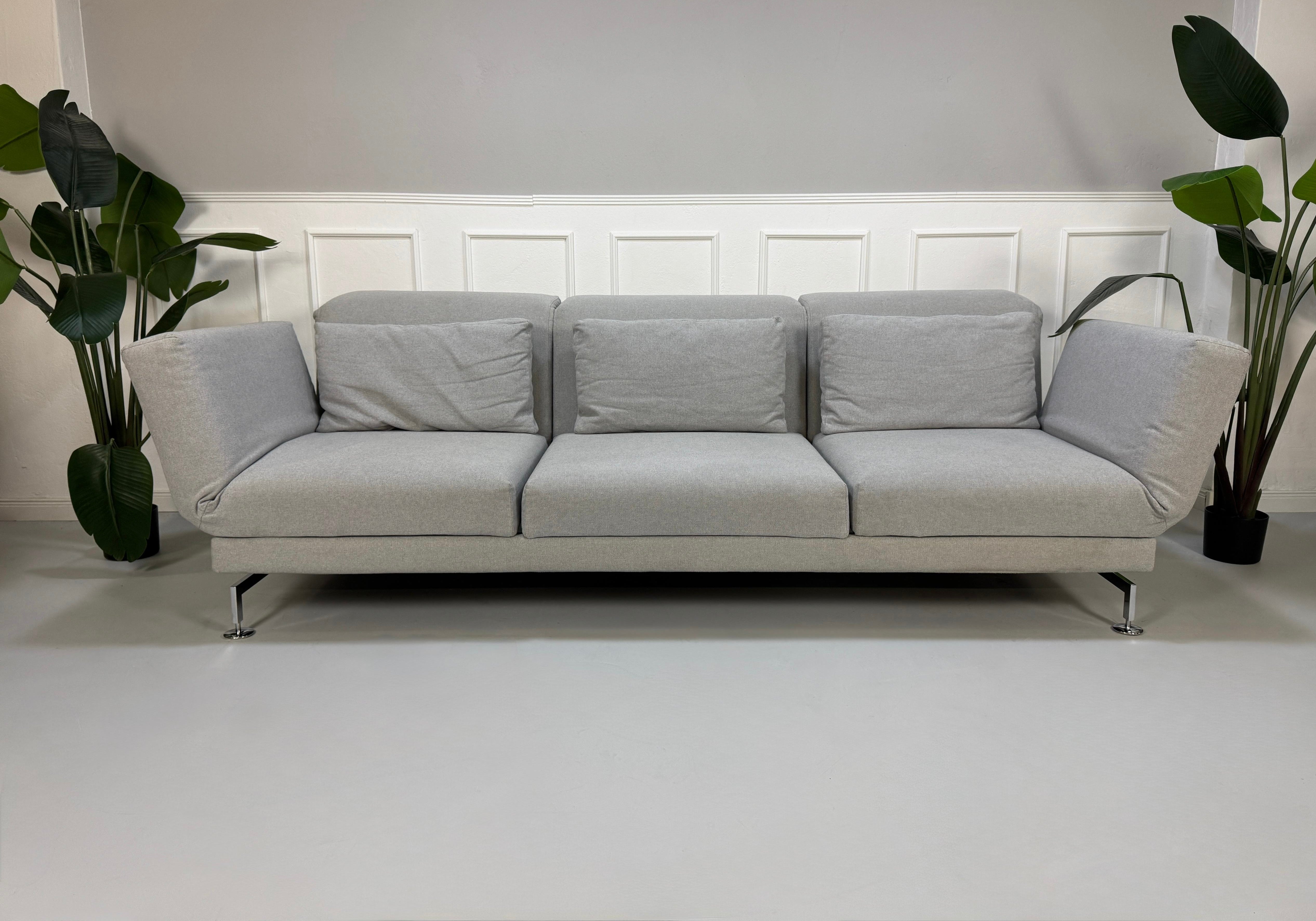 Gebrauchtes graues Brühl Moule Designer Stoff Sofa vor einer Wand, stilvoll und modern eingerichtet.
