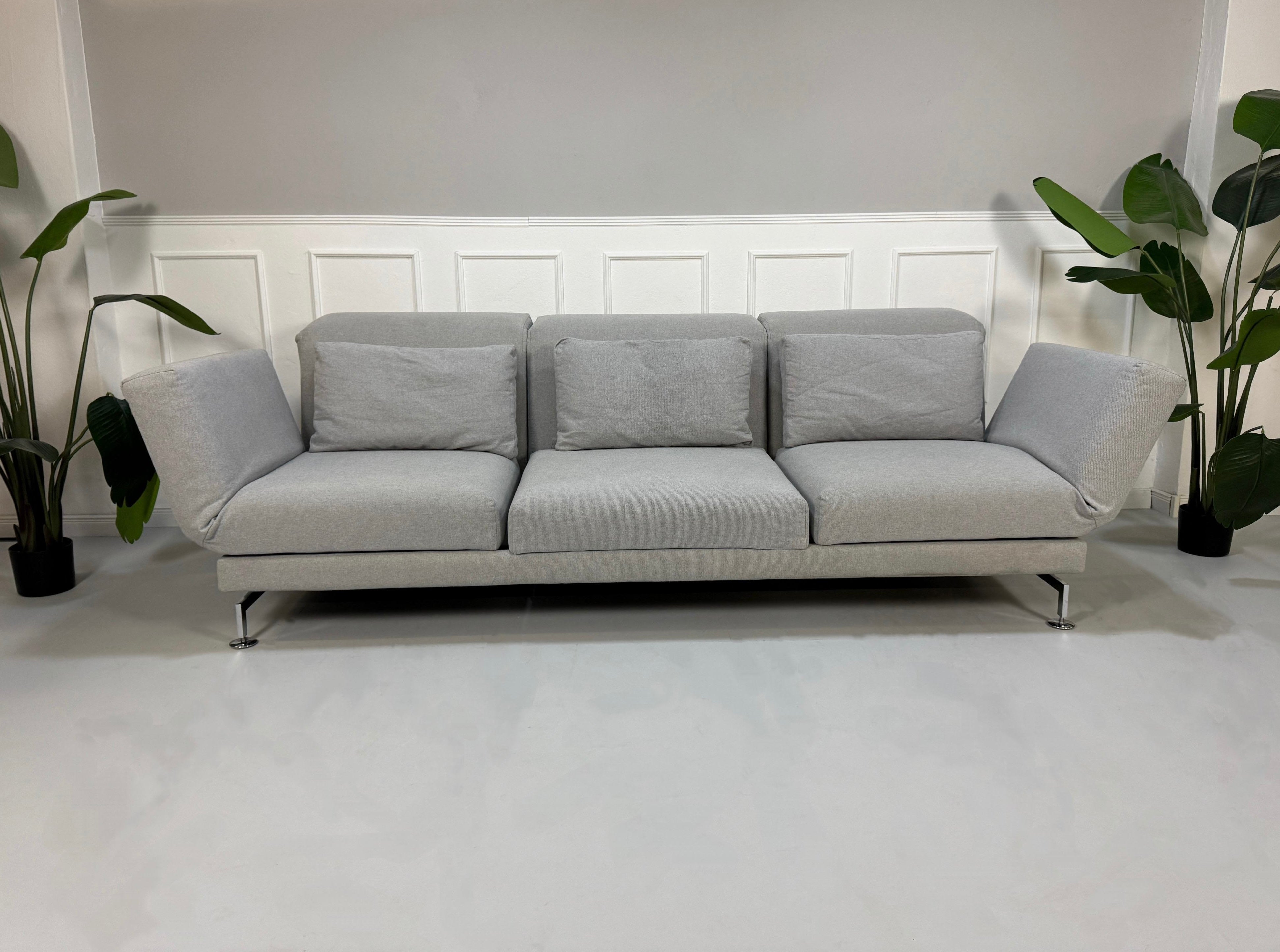 Gebrauchtes graues Brühl Moule Designer Stoff Sofa vor einer Wand, stilvoll und modern eingerichtet.