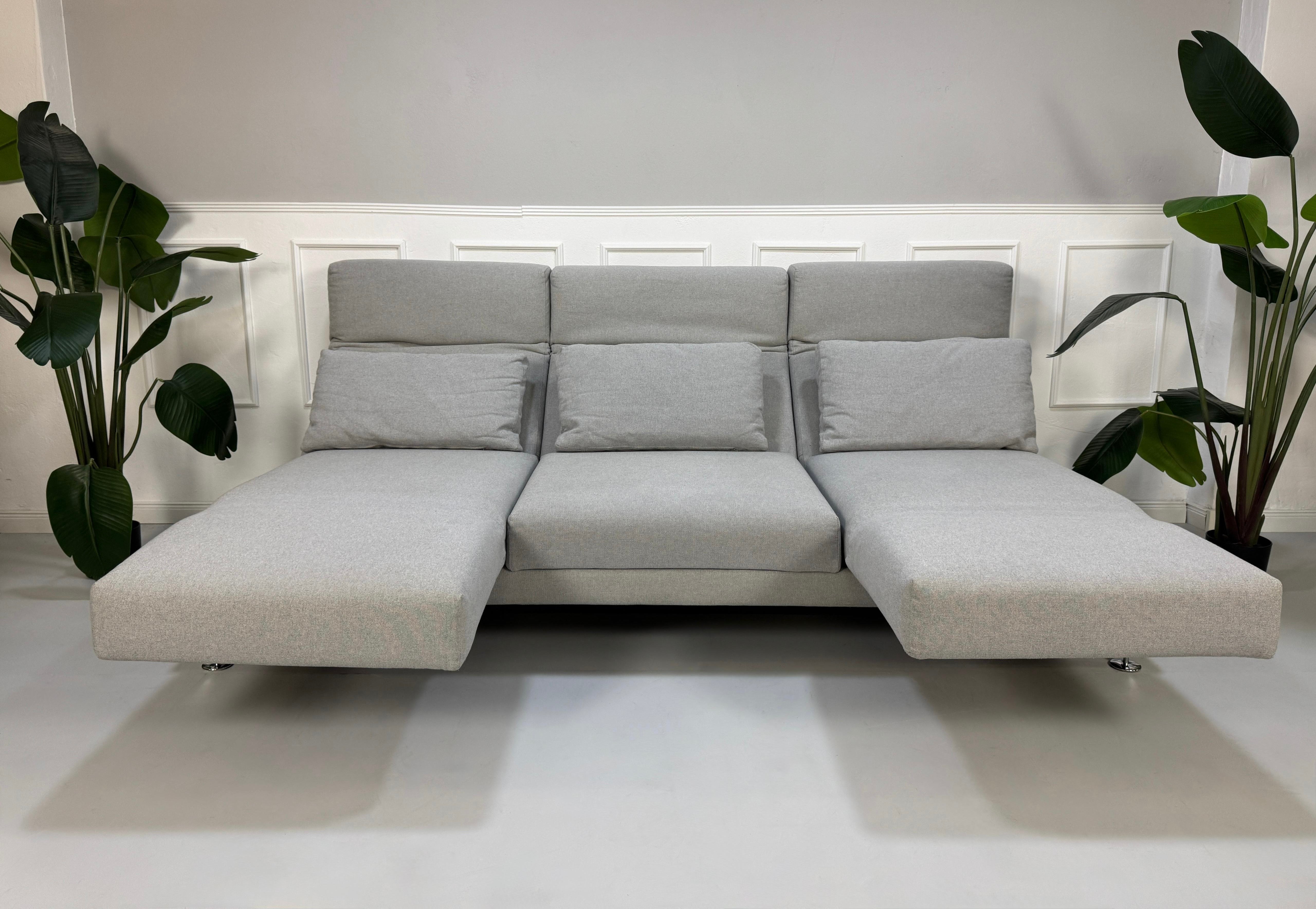 Gebrauchtes graues Brühl Moule Designer Stoff Sofa vor einer Wand, stilvoll und modern eingerichtet.