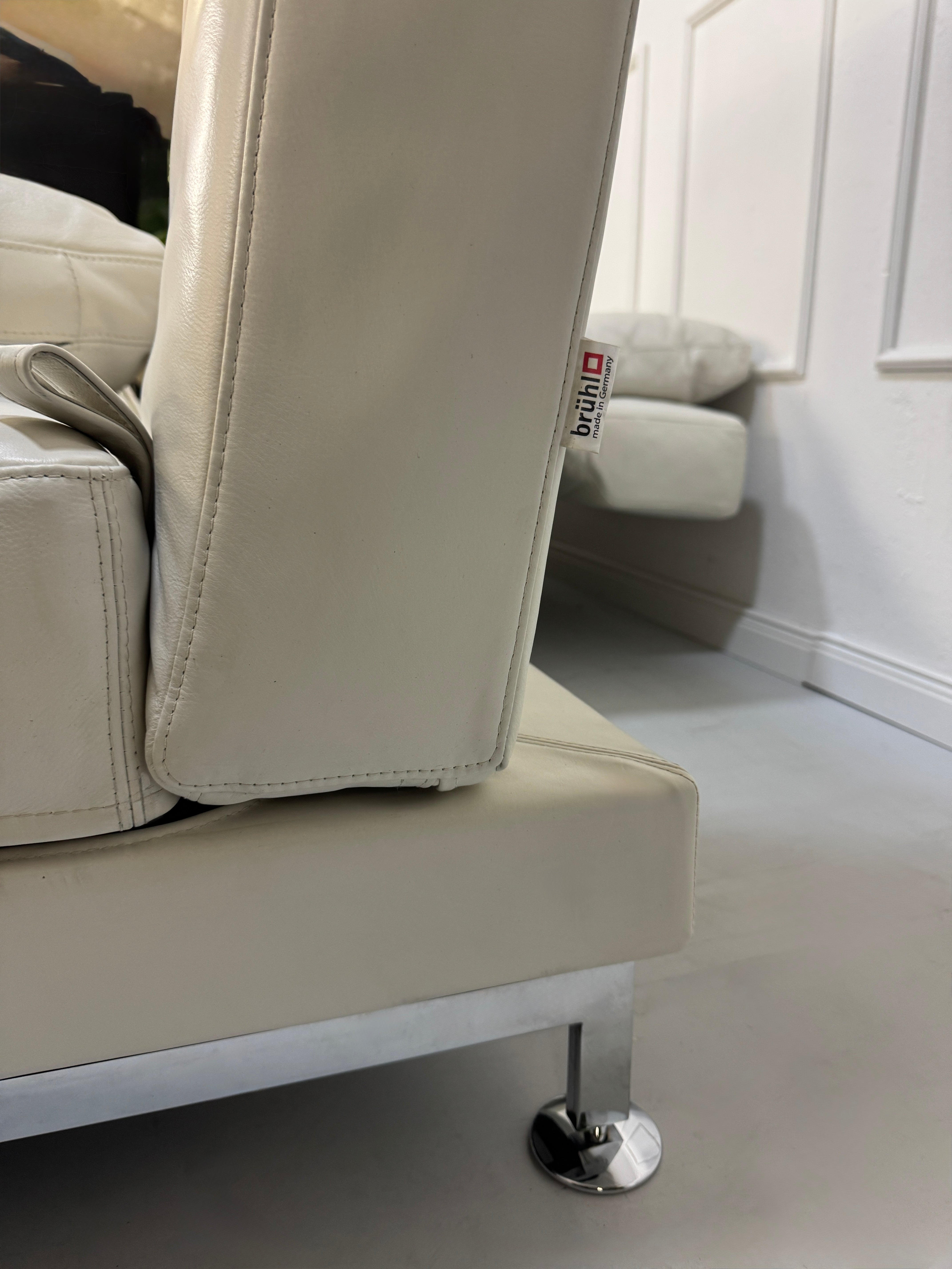 Gebrauchtes weißes Brühl Moule Designer Leder Sofa vor einer Wand, stilvoll und modern eingerichtet.