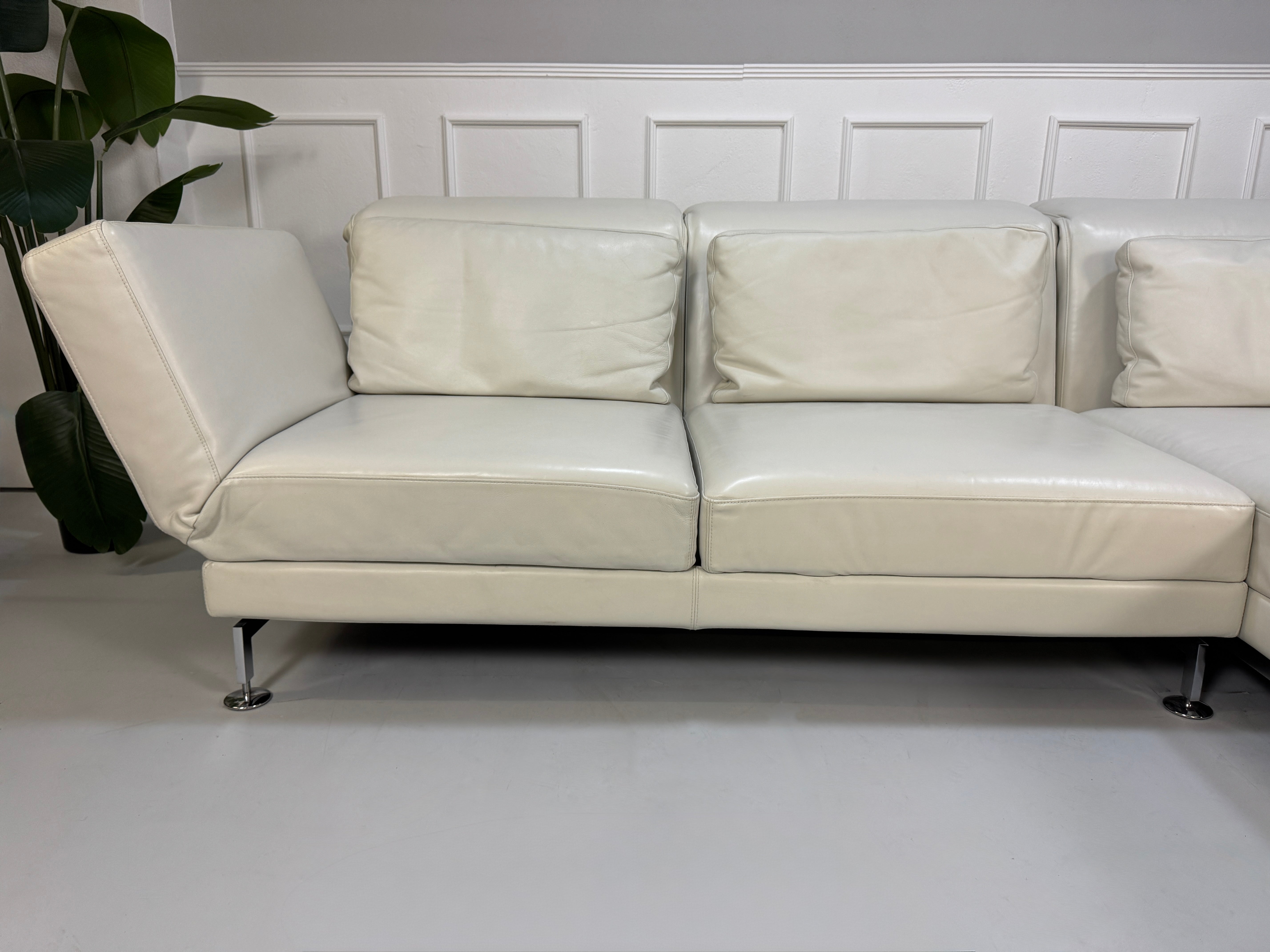 Gebrauchtes weißes Brühl Moule Designer Leder Sofa vor einer Wand, stilvoll und modern eingerichtet.