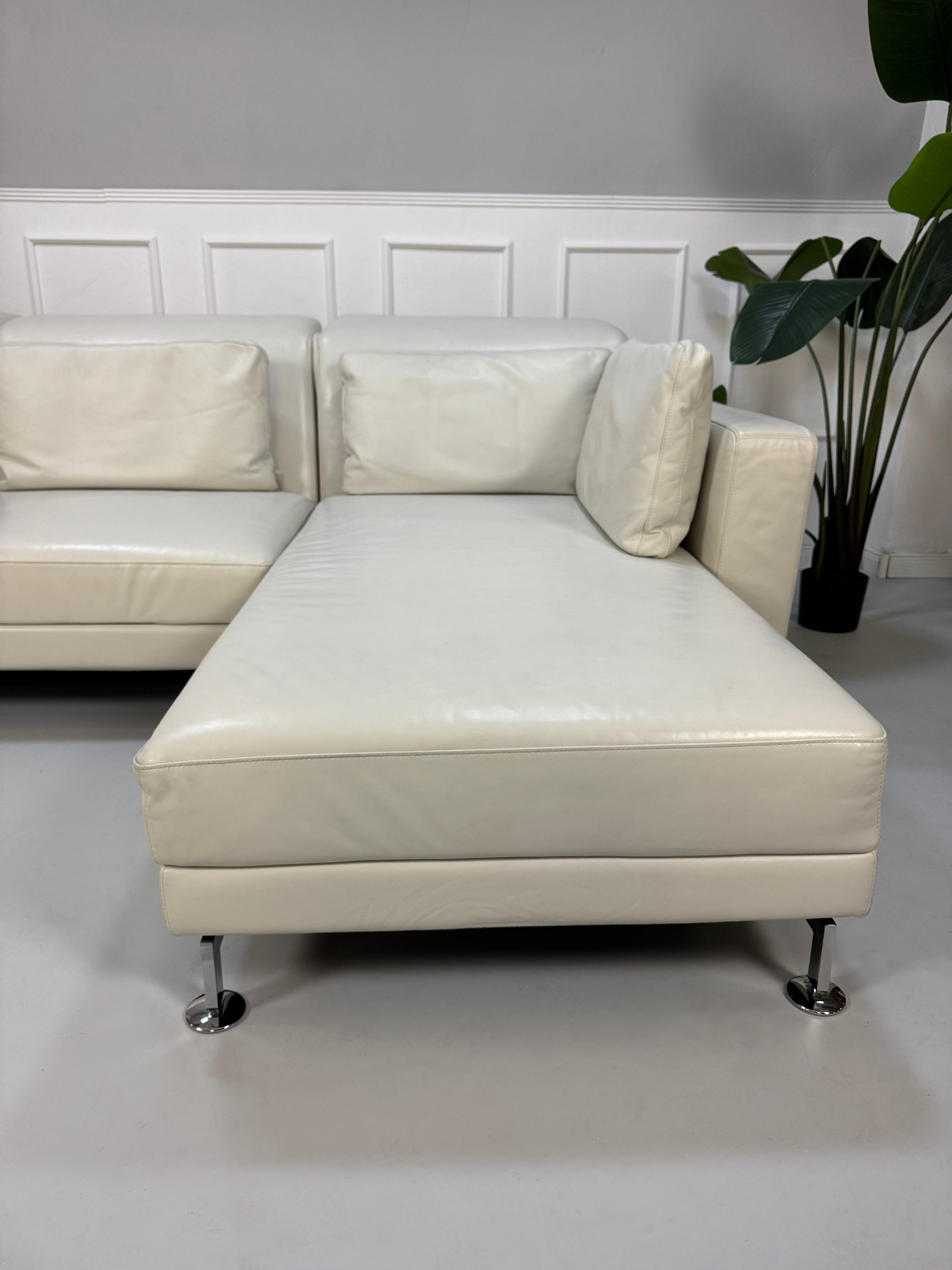 Gebrauchtes weißes Brühl Moule Designer Leder Sofa vor einer Wand, stilvoll und modern eingerichtet.