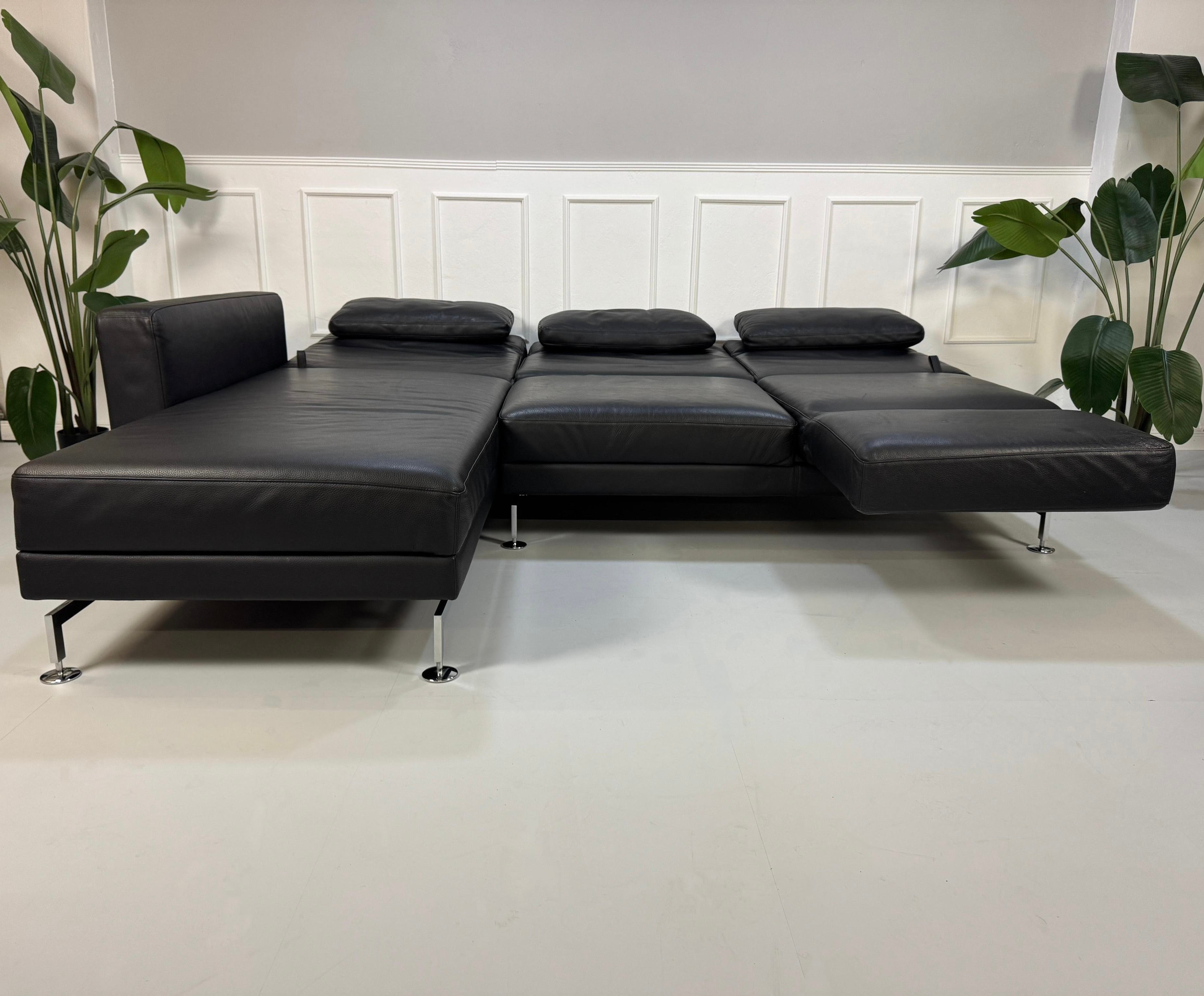 Gebrauchtes schwarzes Brühl Moule Designer Leder Sofa vor einer Wand, stilvoll und modern eingerichtet.