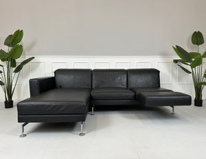 Gebrauchtes schwarzes Brühl Moule Designer Leder Sofa vor einer Wand, stilvoll und modern eingerichtet.