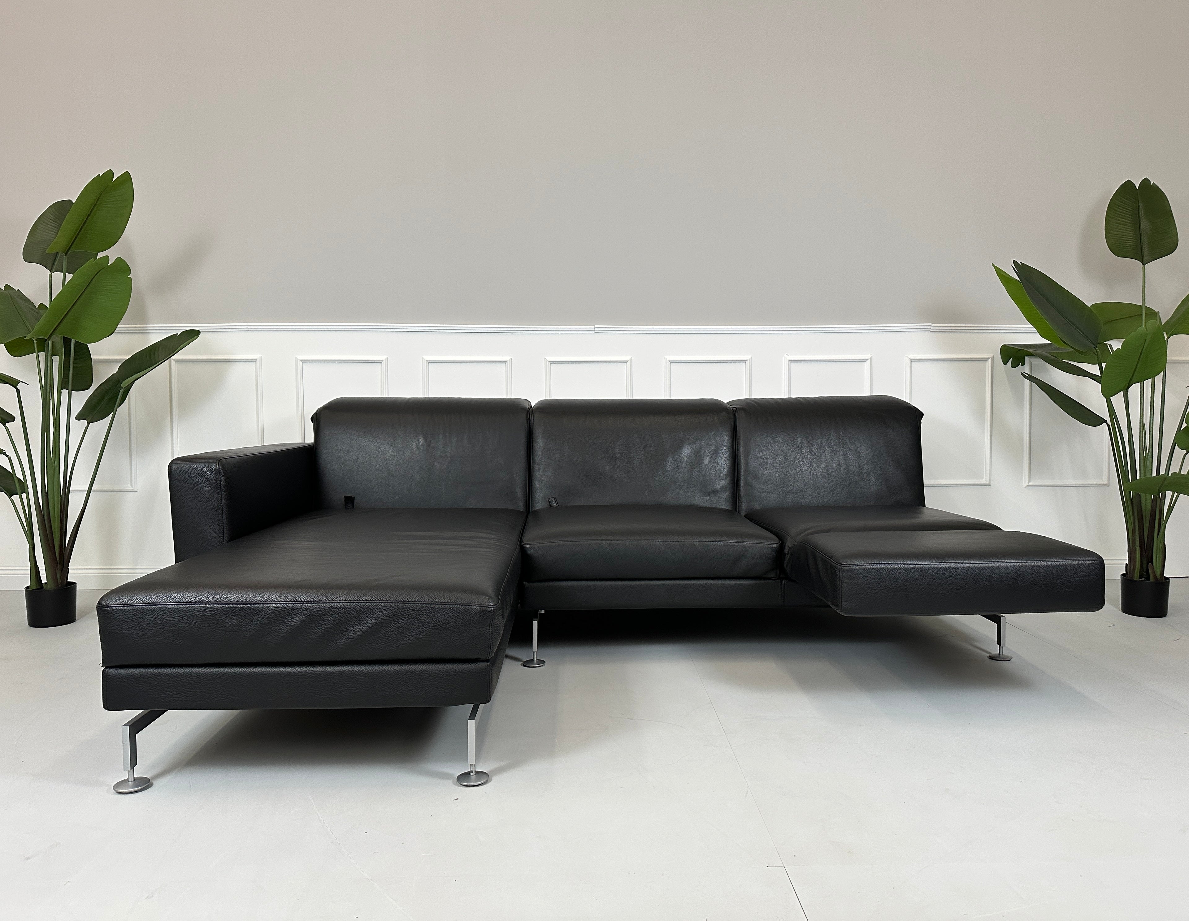 Gebrauchtes schwarzes Brühl Moule Designer Leder Sofa vor einer Wand, stilvoll und modern eingerichtet.