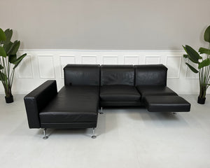 Gebrauchtes schwarzes Brühl Moule Designer Leder Sofa vor einer Wand, stilvoll und modern eingerichtet.