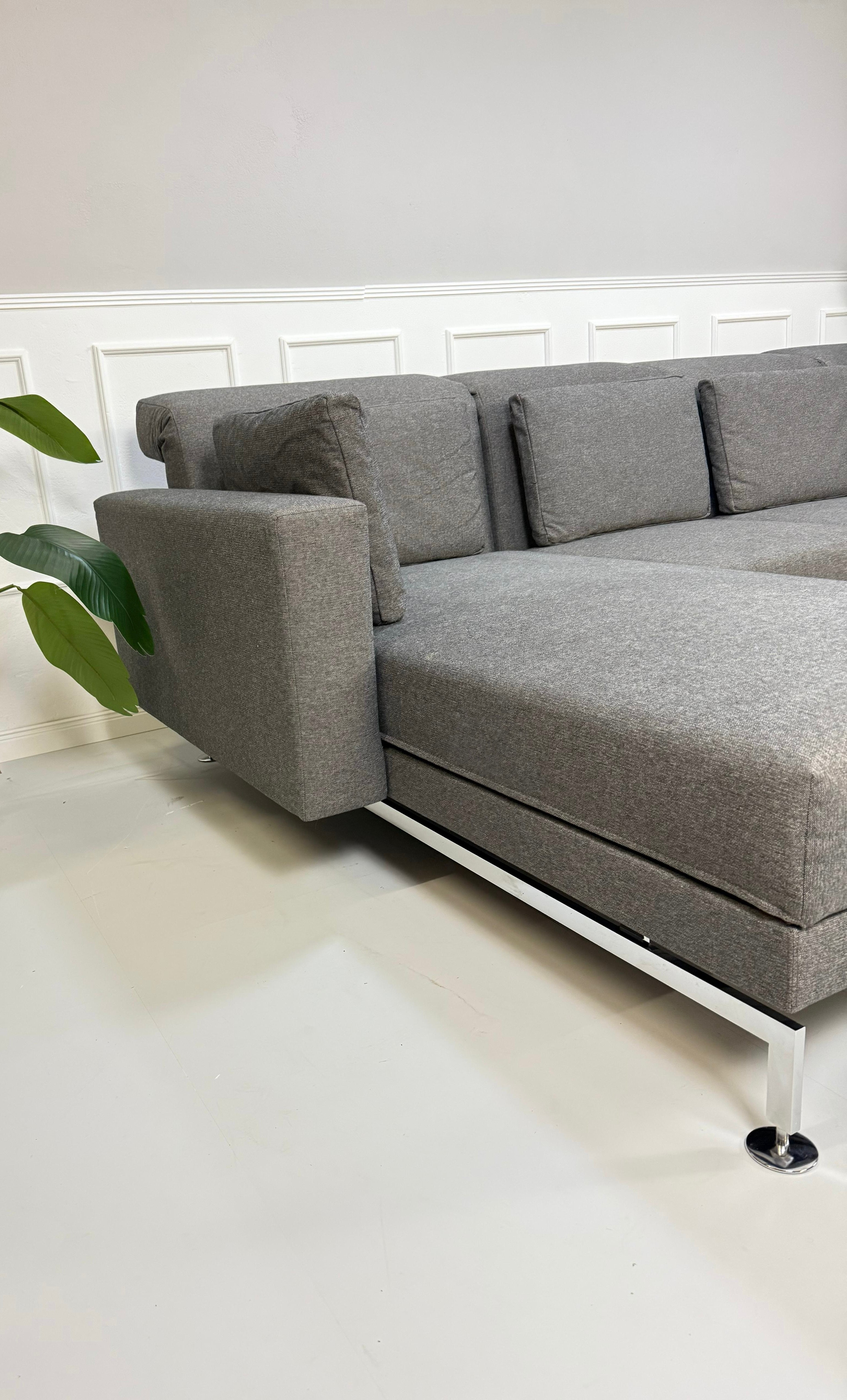 Gebrauchtes graues Brühl Moule Small Designer Stoff Sofa vor einer Wand, stilvoll und modern eingerichtet.