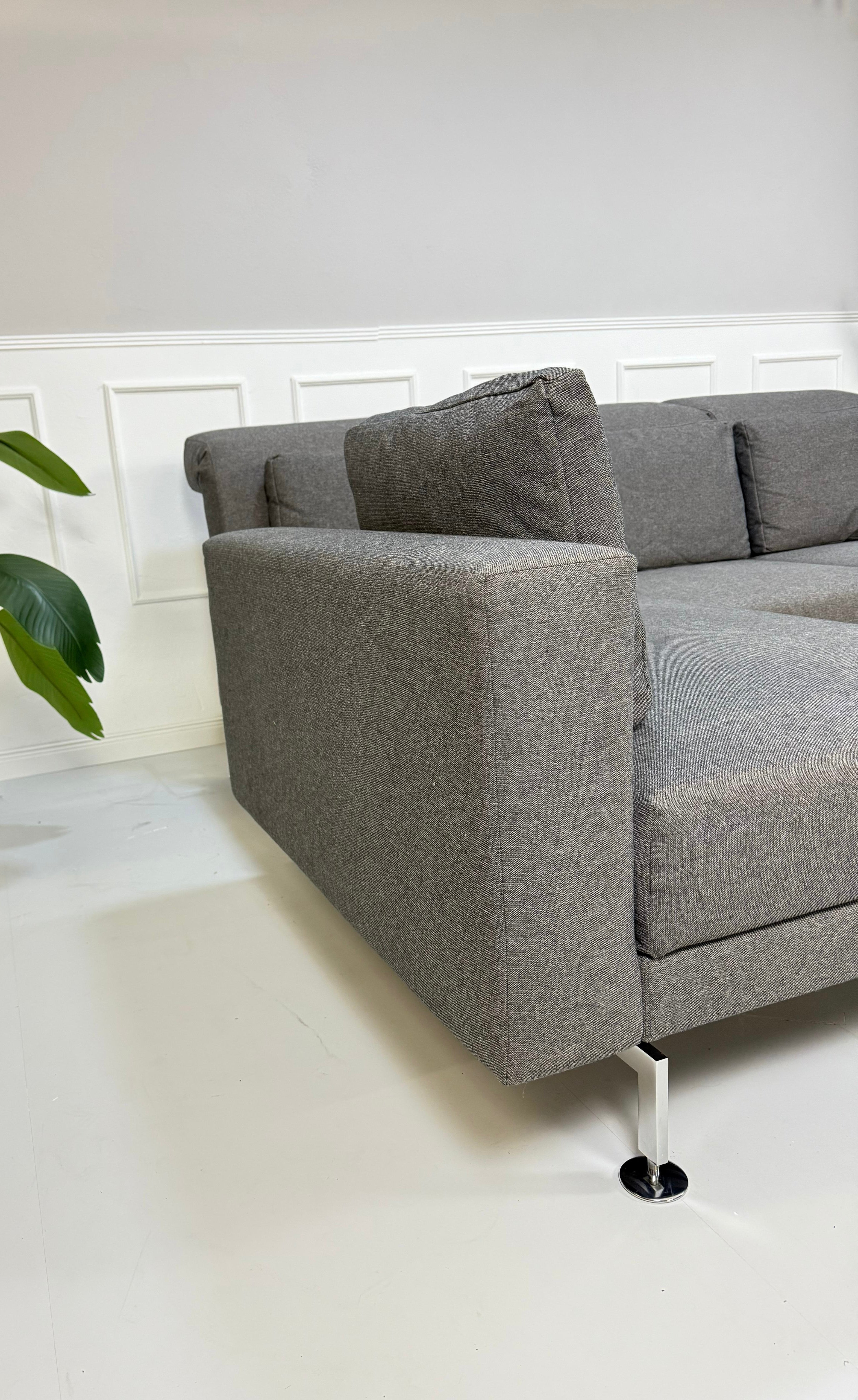 Gebrauchtes graues Brühl Moule Small Designer Stoff Sofa vor einer Wand, stilvoll und modern eingerichtet.