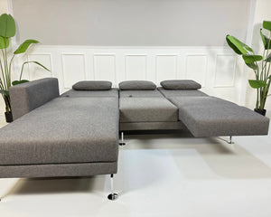 Gebrauchtes graues Brühl Moule Small Designer Stoff Sofa vor einer Wand, stilvoll und modern eingerichtet.