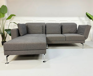 Gebrauchtes graues Brühl Moule Small Designer Stoff Sofa vor einer Wand, stilvoll und modern eingerichtet.