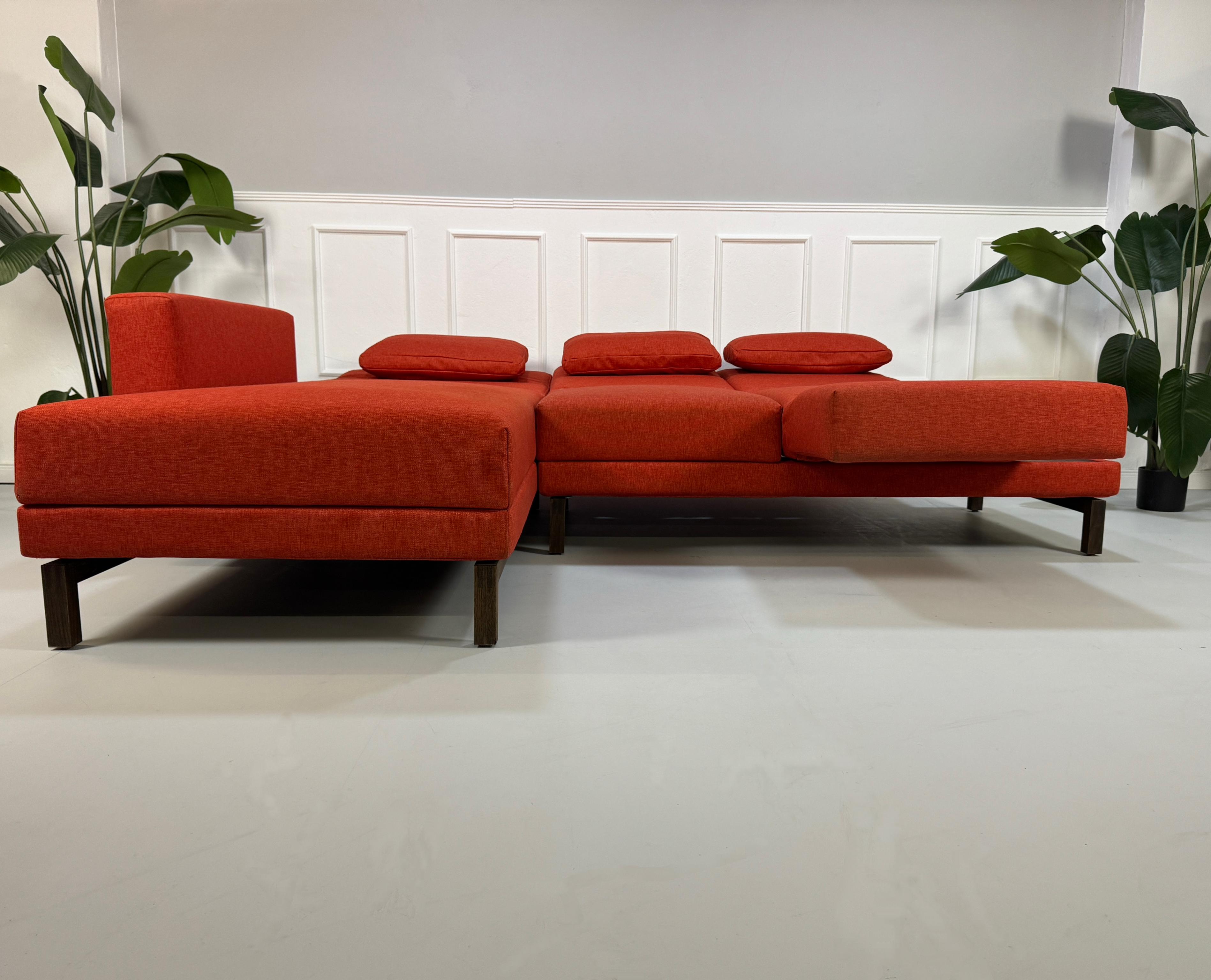 Gebrauchtes orangen Brühl Moule Small Designer Stoff Sofa vor einer Wand, stilvoll und modern eingerichtet.
