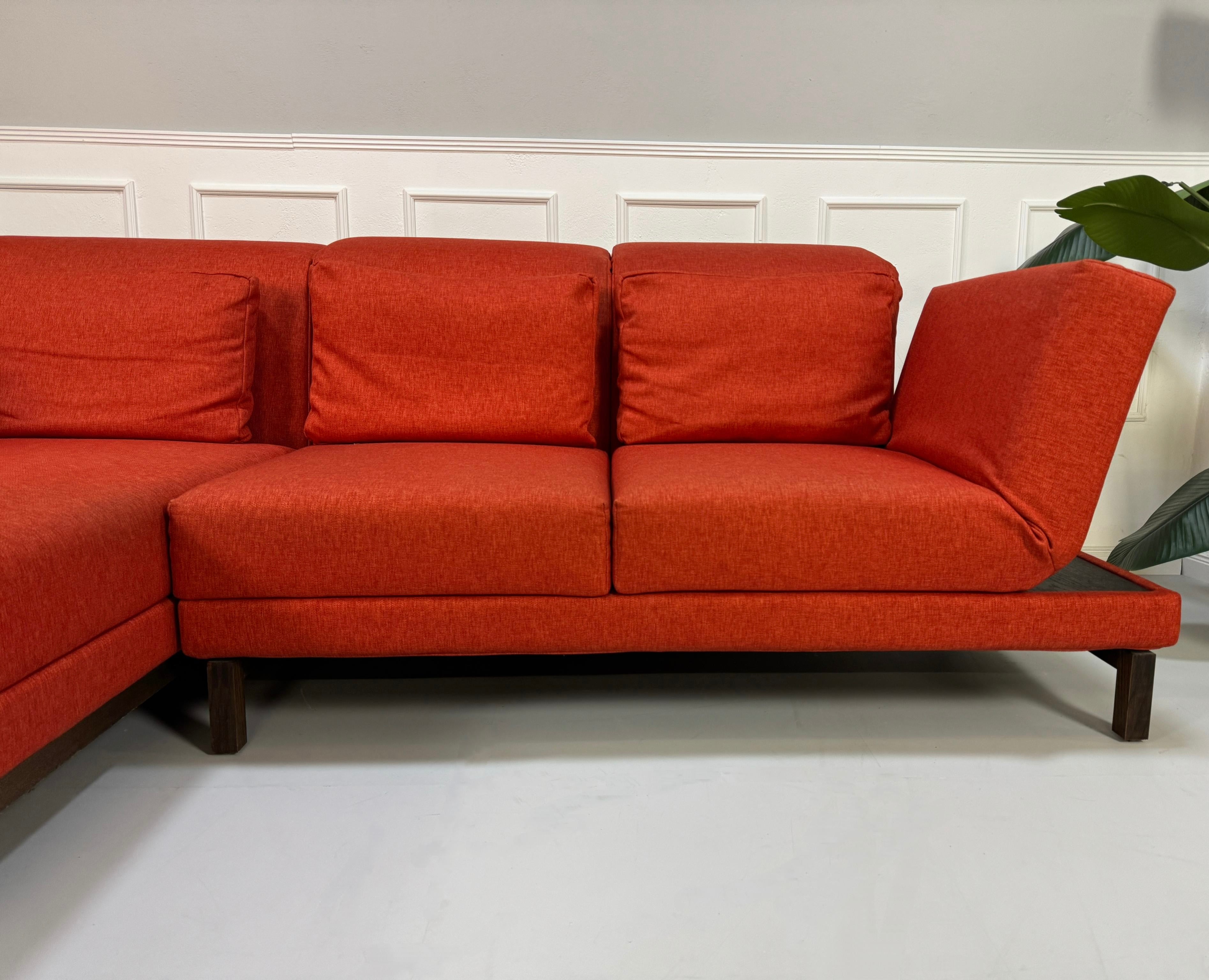 Gebrauchtes orangen Brühl Moule Small Designer Stoff Sofa vor einer Wand, stilvoll und modern eingerichtet.