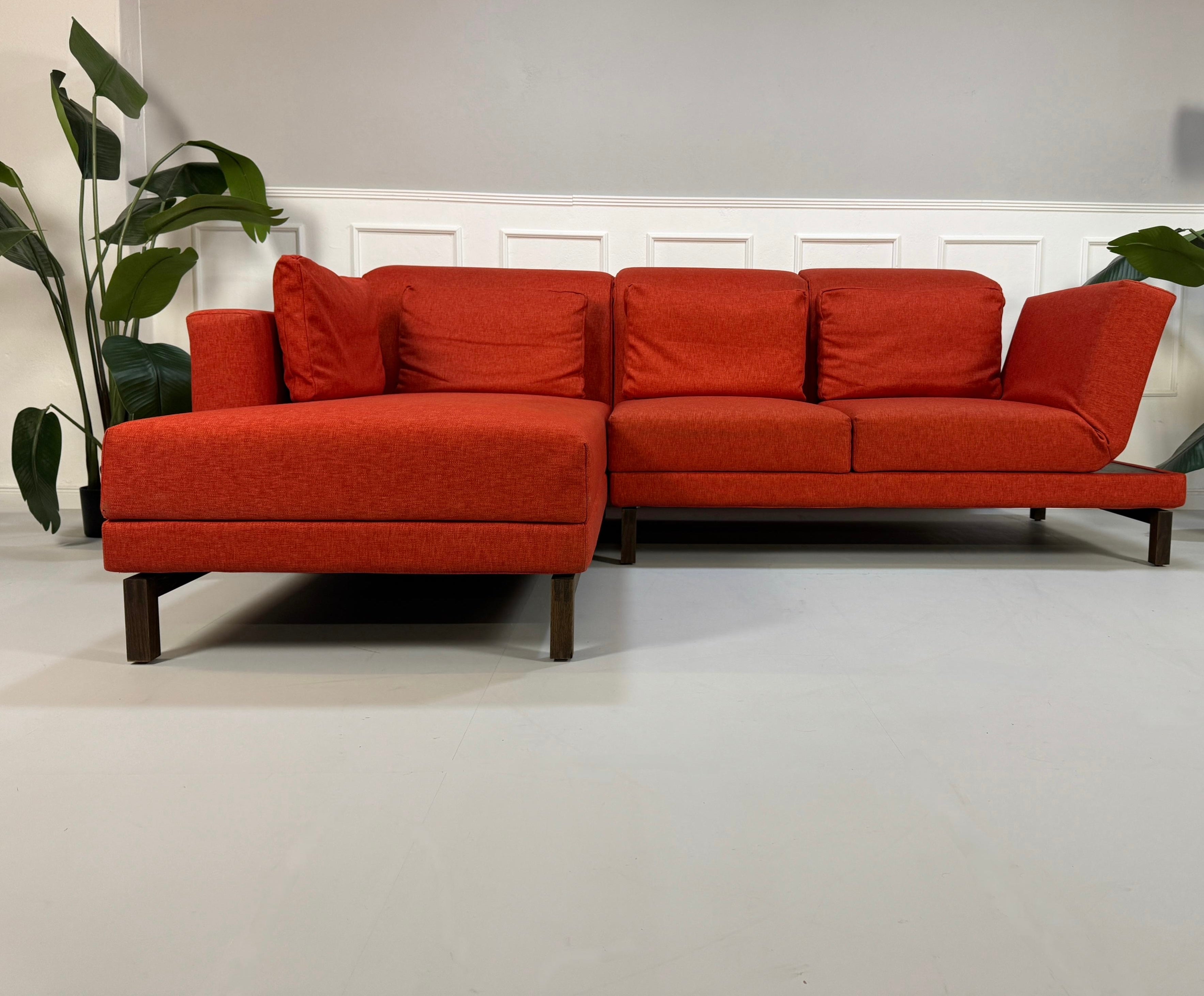 Gebrauchtes orangen Brühl Moule Small Designer Stoff Sofa vor einer Wand, stilvoll und modern eingerichtet.