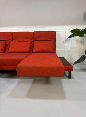 Gebrauchtes orangen Brühl Moule Small Designer Stoff Sofa vor einer Wand, stilvoll und modern eingerichtet.