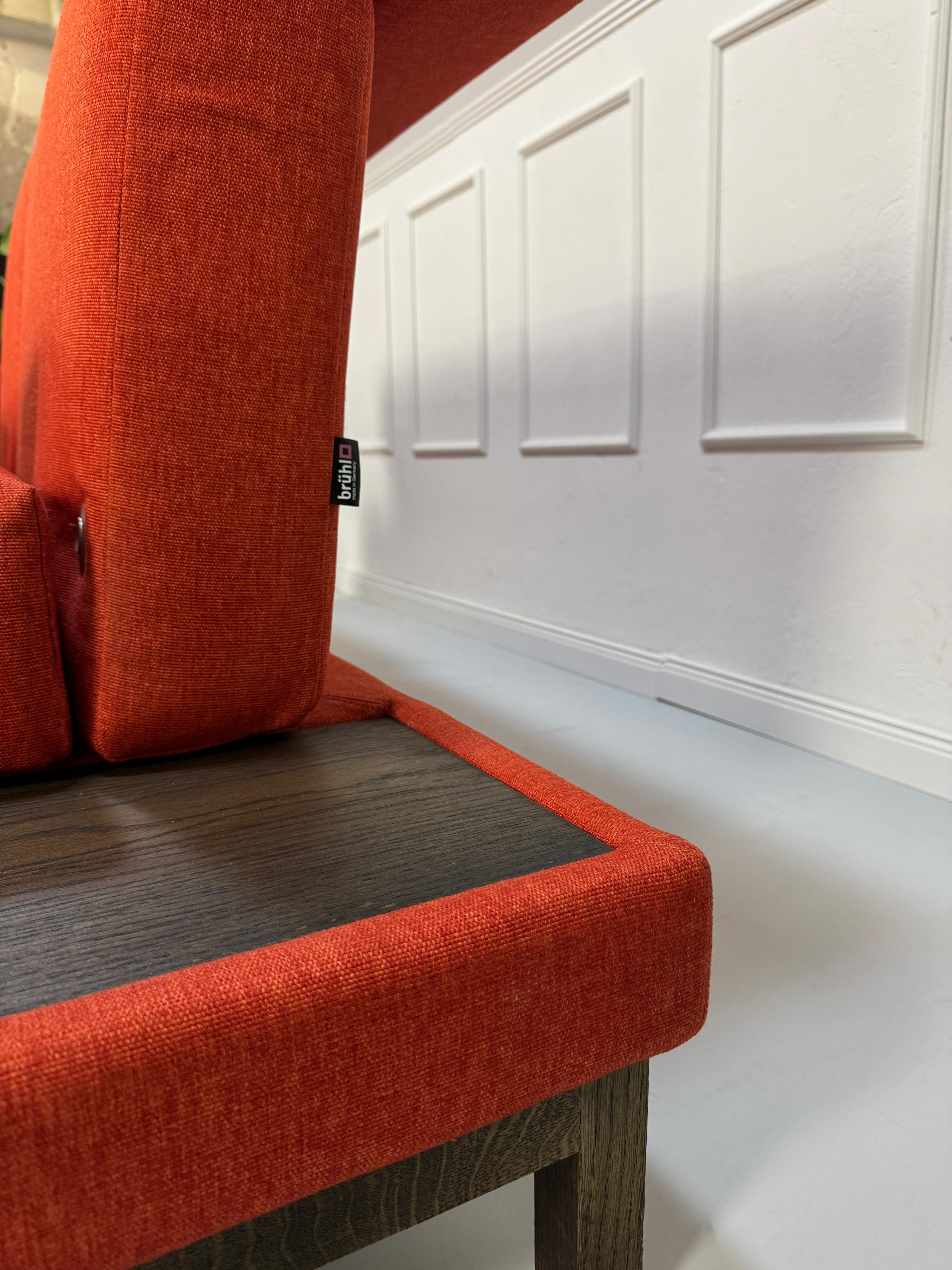Gebrauchtes orangen Brühl Moule Small Designer Stoff Sofa vor einer Wand, stilvoll und modern eingerichtet.