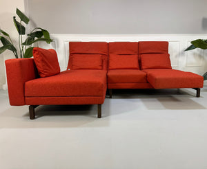 Gebrauchtes orangen Brühl Moule Small Designer Stoff Sofa vor einer Wand, stilvoll und modern eingerichtet.