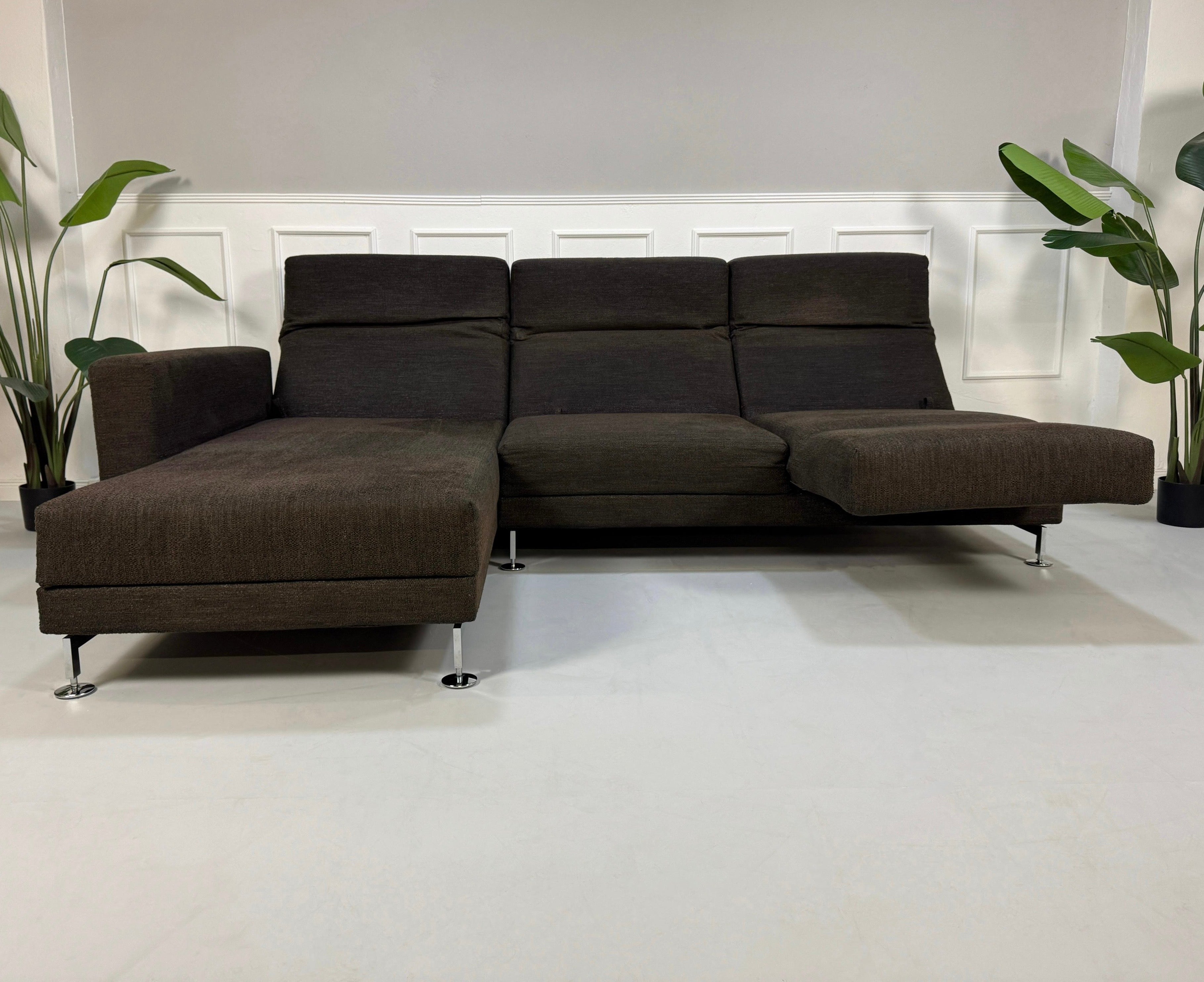 Gebrauchtes braunes Brühl Moule Designer Stoff Sofa vor einer Wand, stilvoll und modern eingerichtet.