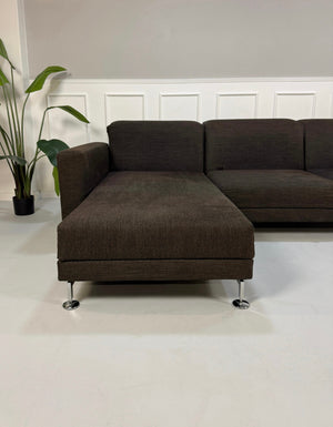 Gebrauchtes braunes Brühl Moule Designer Stoff Sofa vor einer Wand, stilvoll und modern eingerichtet.