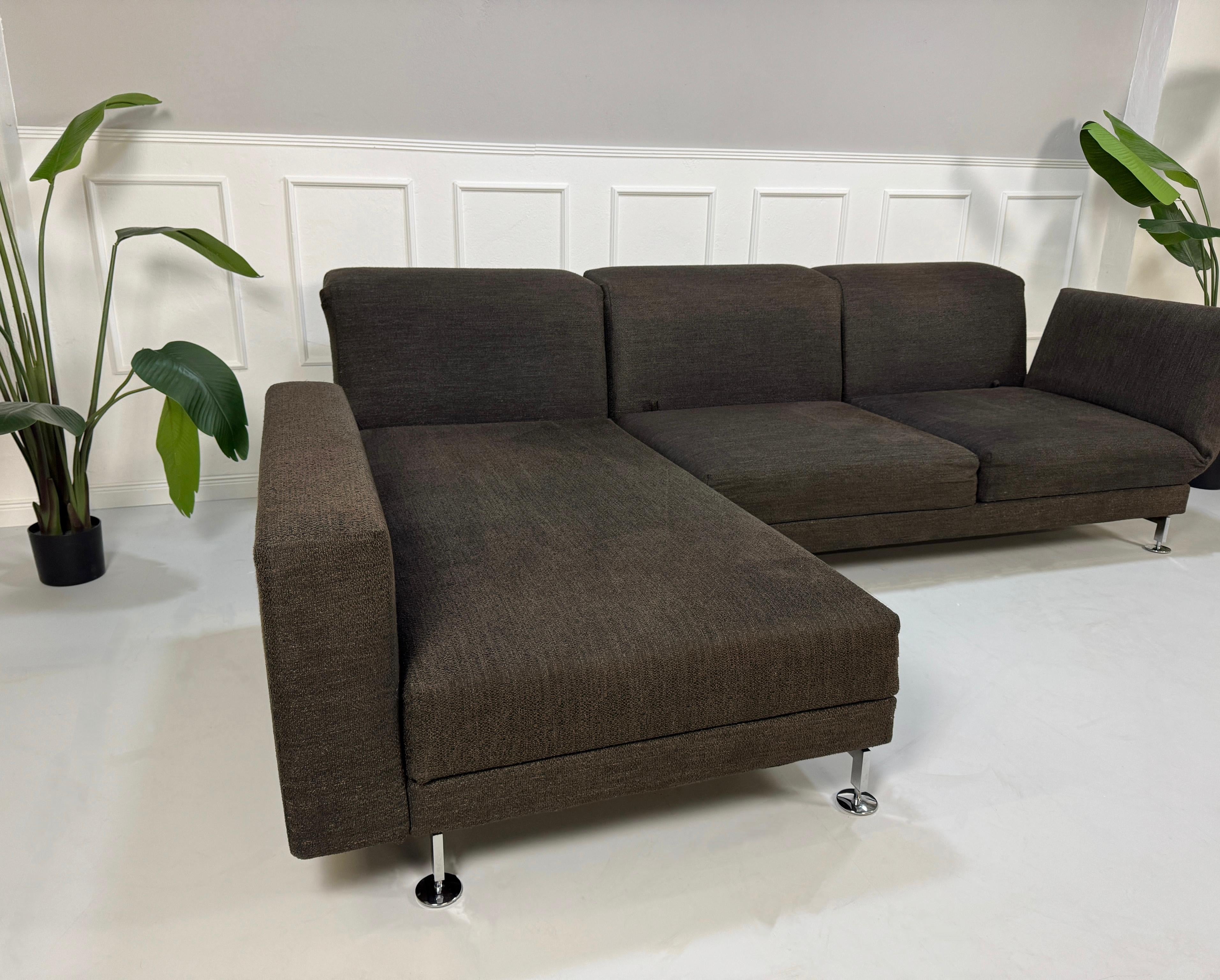 Gebrauchtes braunes Brühl Moule Designer Stoff Sofa vor einer Wand, stilvoll und modern eingerichtet.