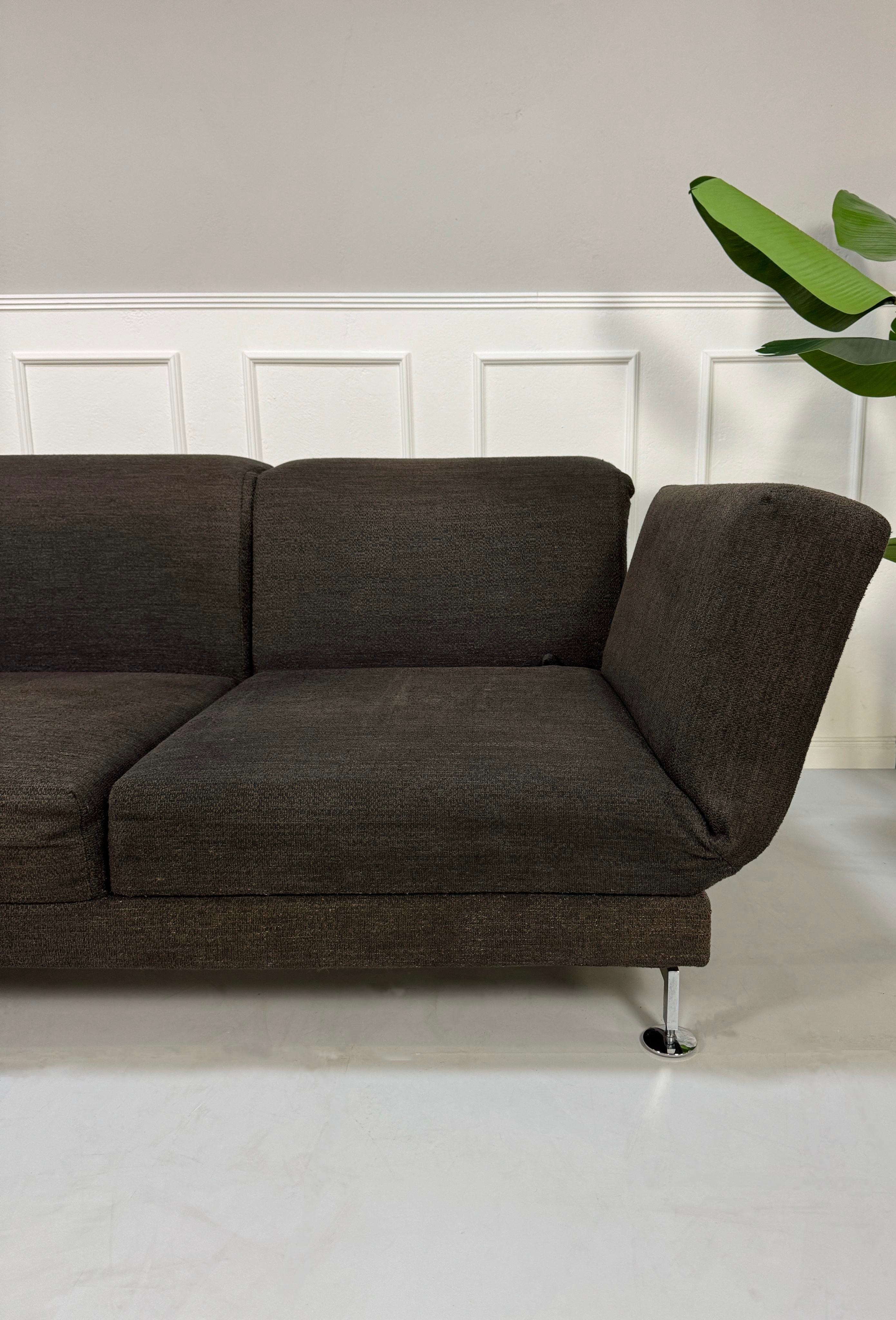 Gebrauchtes braunes Brühl Moule Designer Stoff Sofa vor einer Wand, stilvoll und modern eingerichtet.