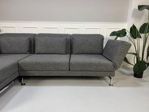 Ein graues Brühl Moule Designer Stoff Sofa vor einer Wand, stilvoll und modern eingerichtet.