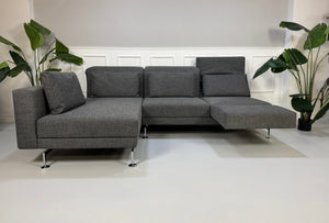 Ein graues Brühl Moule Designer Stoff Sofa vor einer Wand, stilvoll und modern eingerichtet.