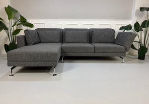 Ein graues Brühl Moule Designer Stoff Sofa vor einer Wand, stilvoll und modern eingerichtet.
