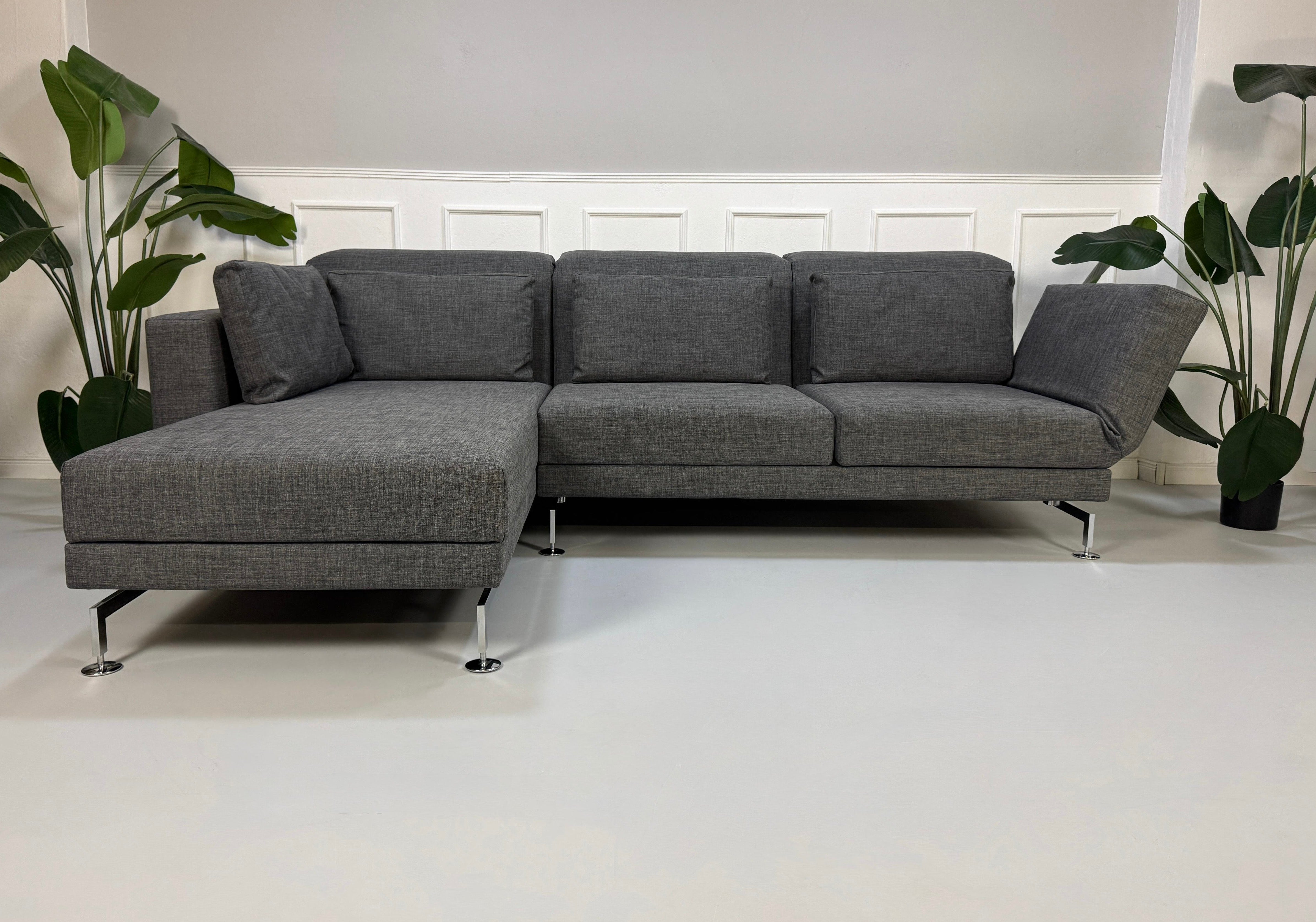 Ein graues Brühl Moule Designer Stoff Sofa vor einer Wand, stilvoll und modern eingerichtet.