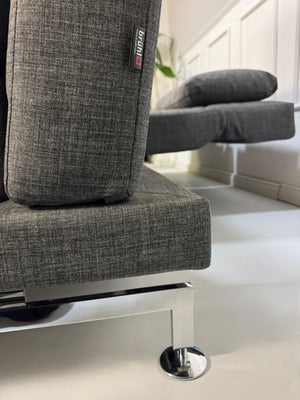 Ein graues Brühl Moule Designer Stoff Sofa vor einer Wand, stilvoll und modern eingerichtet.