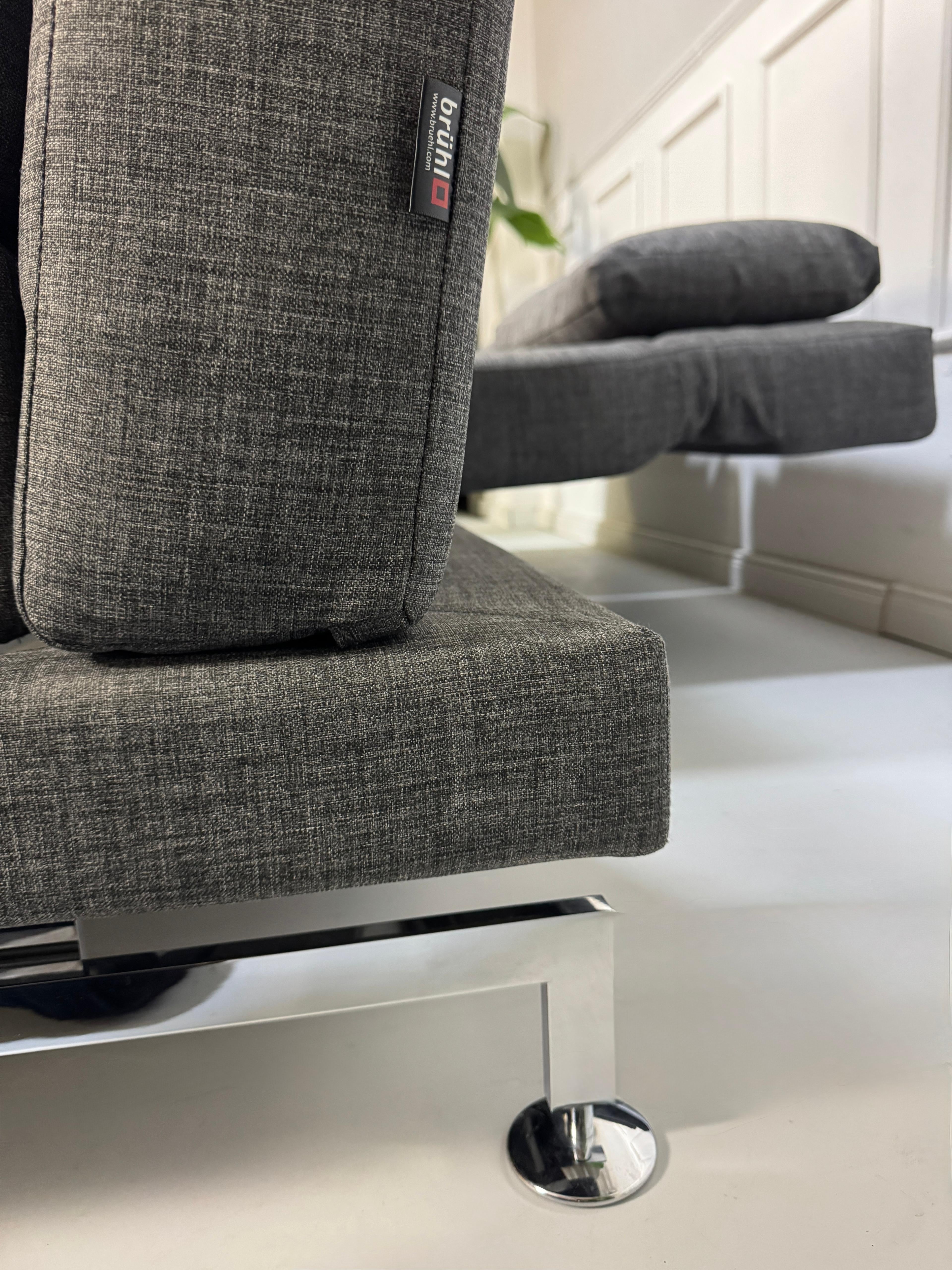 Ein graues Brühl Moule Designer Stoff Sofa vor einer Wand, stilvoll und modern eingerichtet.