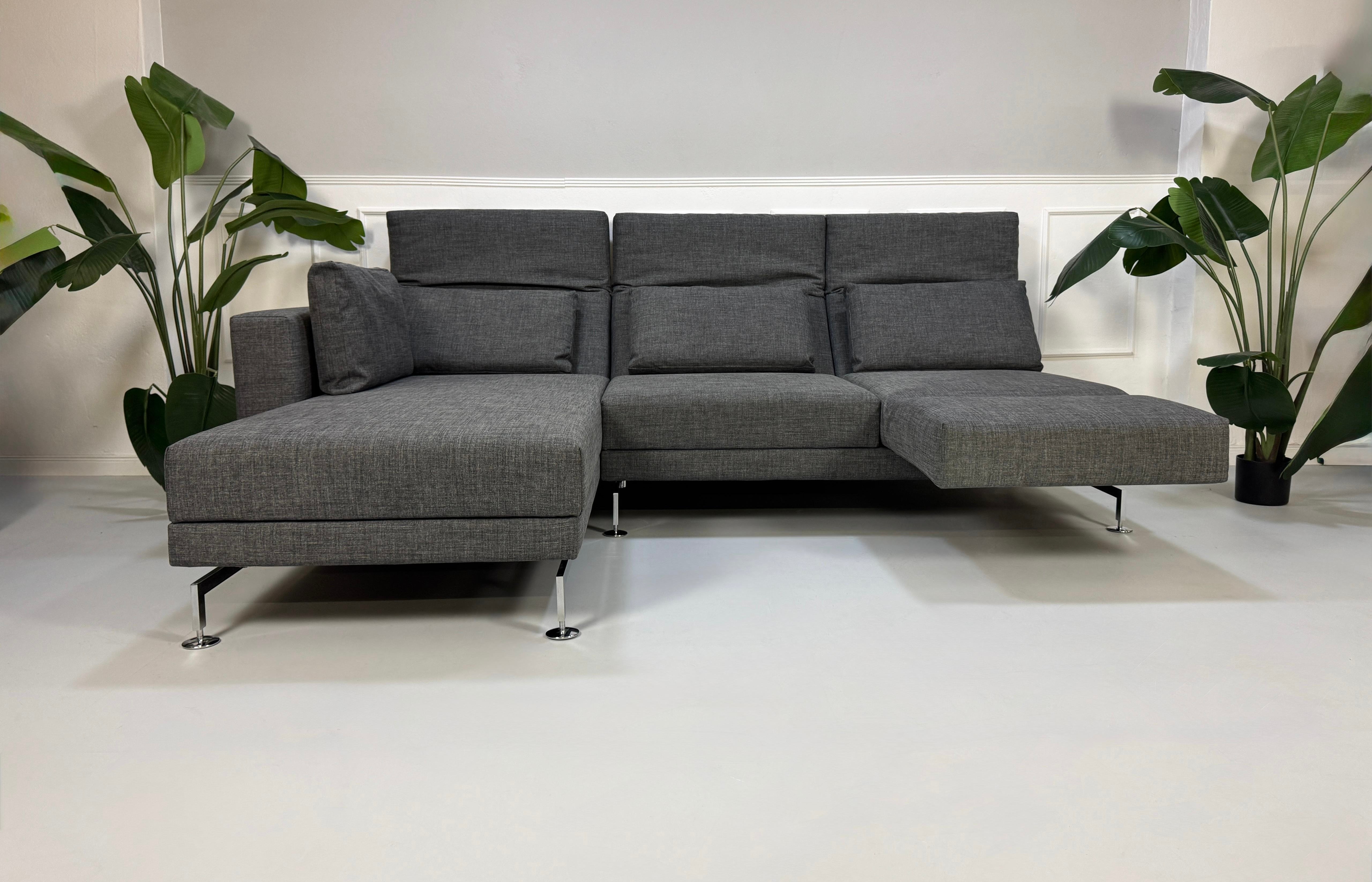 Ein graues Brühl Moule Designer Stoff Sofa vor einer Wand, stilvoll und modern eingerichtet.