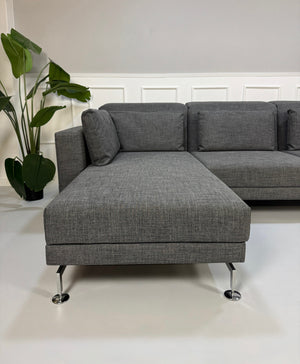 Ein graues Brühl Moule Designer Stoff Sofa vor einer Wand, stilvoll und modern eingerichtet.