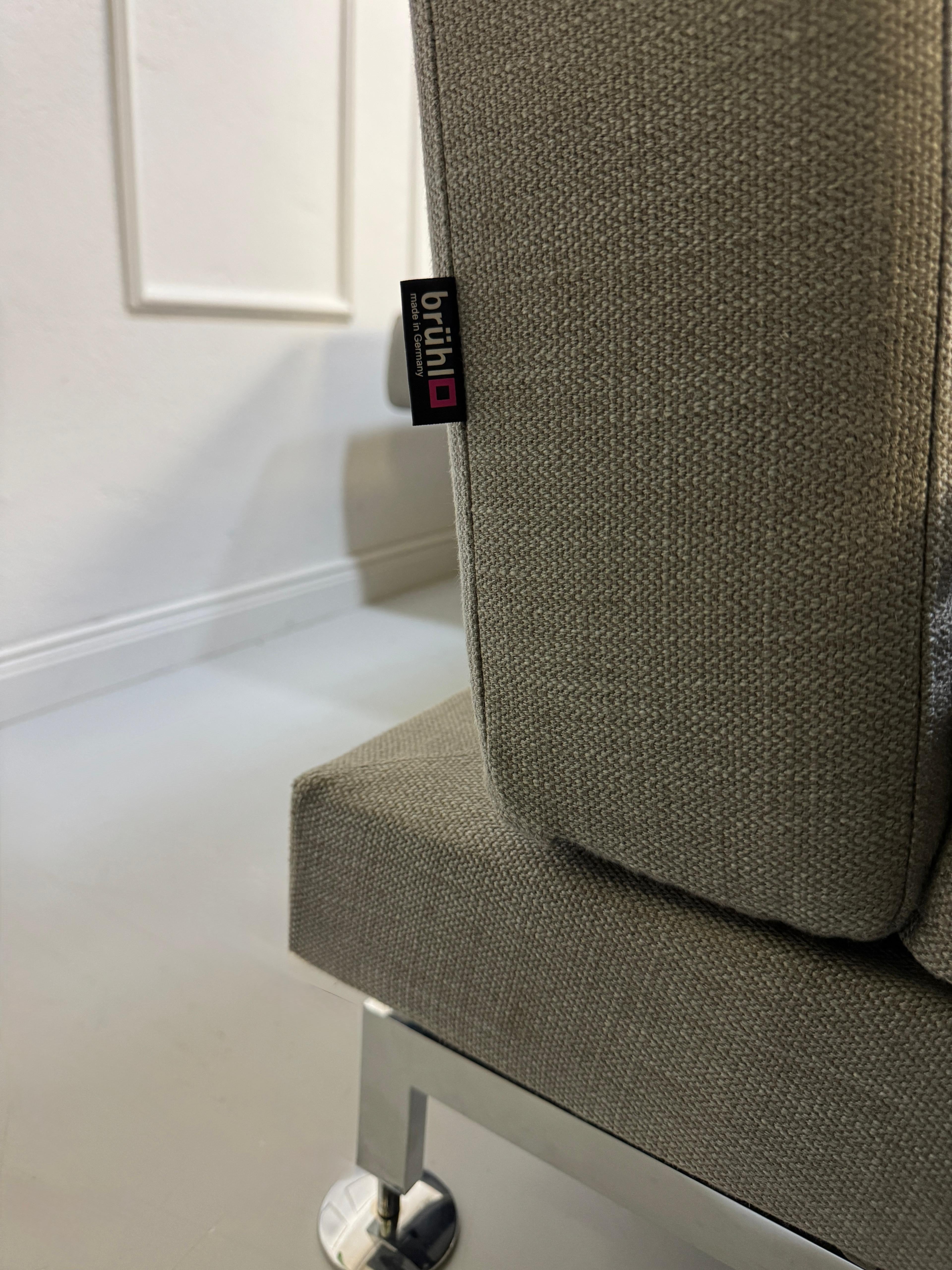Gebrauchtes graues Brühl Moule Designer Stoff Sofa vor einer Wand, stilvoll und modern eingerichtet.