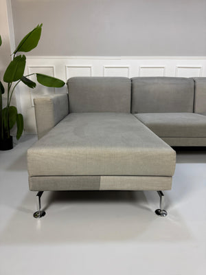 Gebrauchtes graues Brühl Moule Designer Stoff Sofa vor einer Wand, stilvoll und modern eingerichtet.