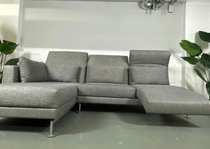 Gebrauchtes Brühl Moule Ecksofa Stoff in der Farbe grau vor einer Wand, stilvoll und modern eingerichtet.