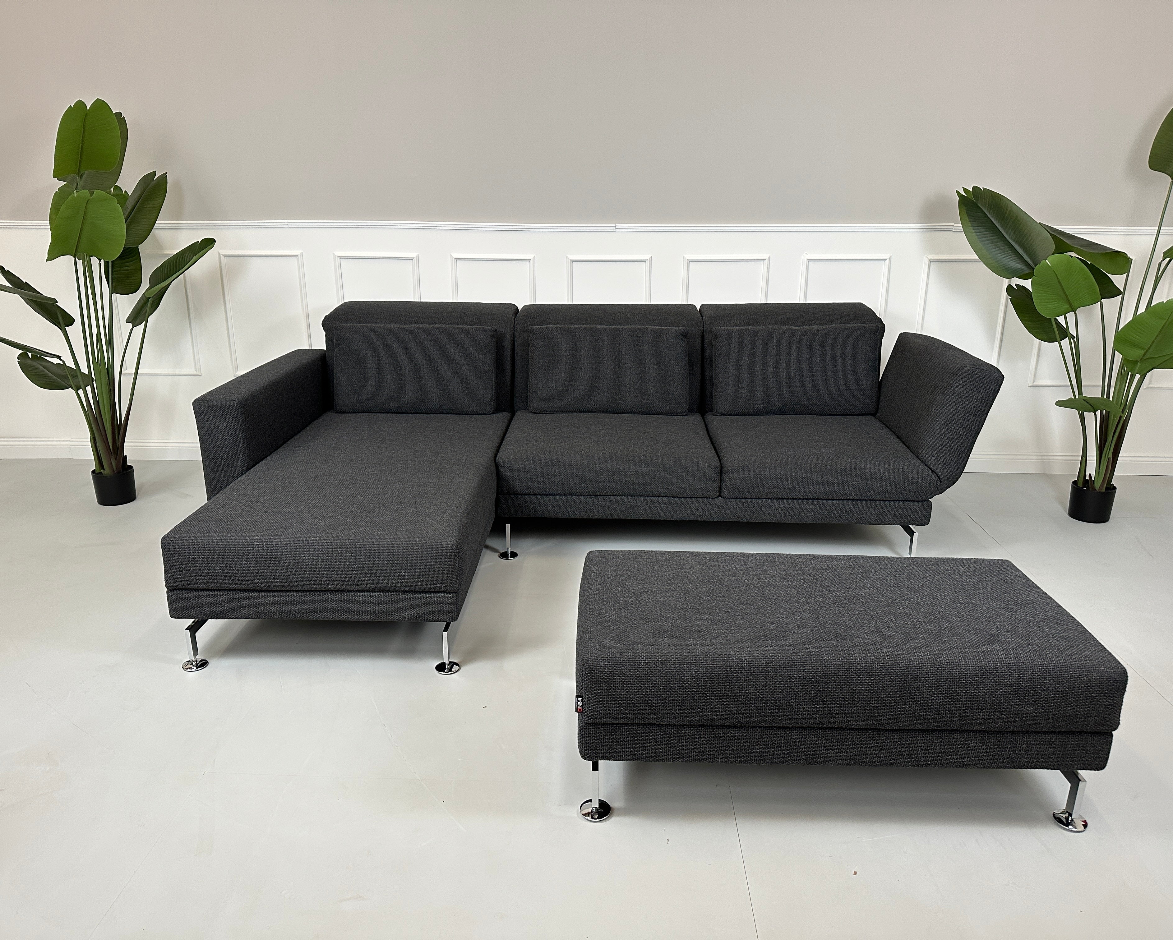 Gebrauchtes graues Brühl Moule Designer Stoff Sofa mit Hocker vor einer Wand, stilvoll und modern eingerichtet.