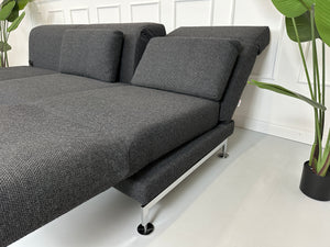 Gebrauchtes graues Brühl Moule Designer Stoff Sofa mit Hocker vor einer Wand, stilvoll und modern eingerichtet.