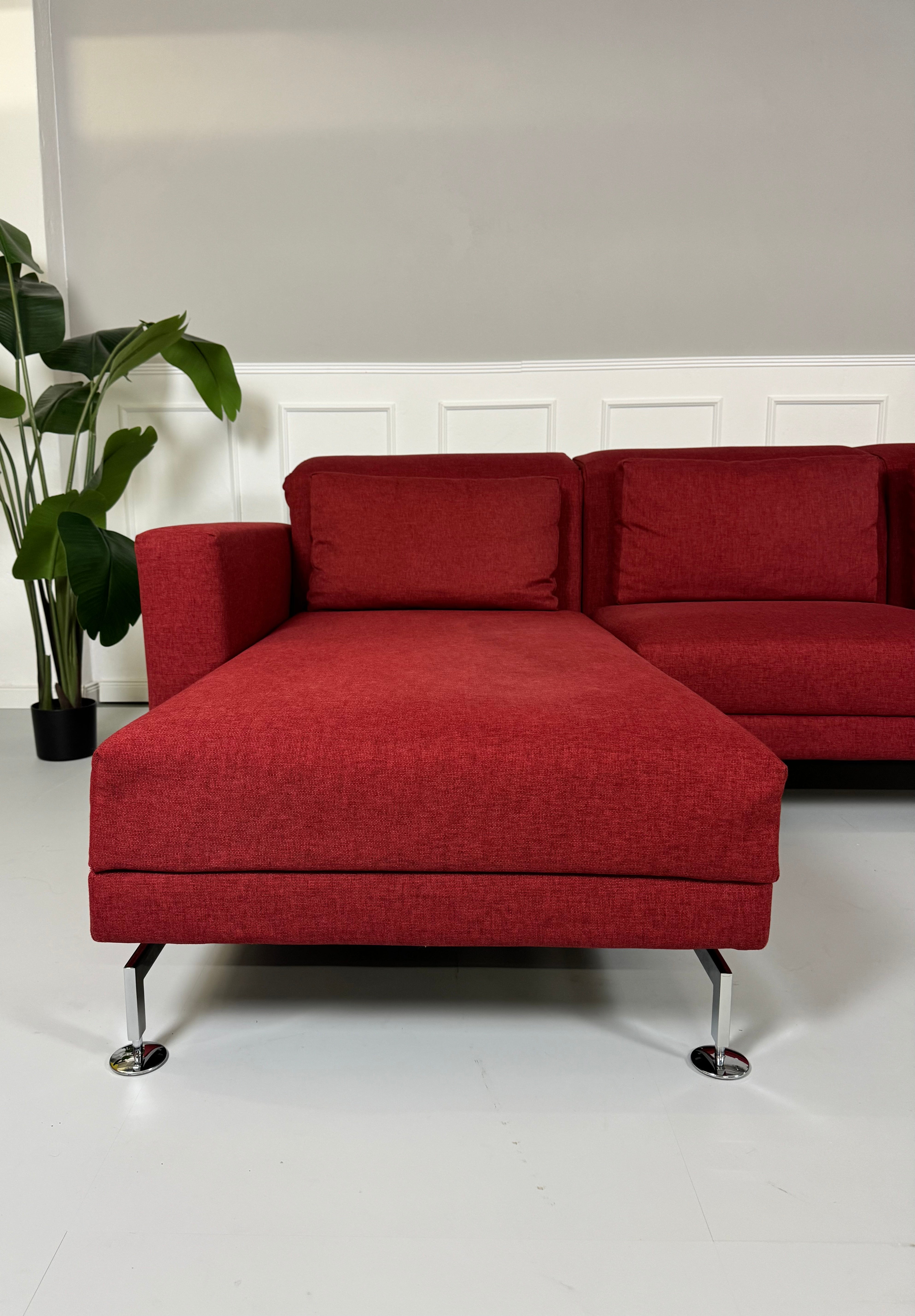 Gebrauchtes Brühl Moule Ecksofa Stoff in der Farbe Rot vor einer Wand, stilvoll und modern eingerichtet.