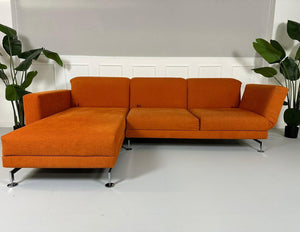 Gebrauchtes Brühl Moule Ecksofa Stoff in der Farbe Orange vor einer Wand, stilvoll und modern eingerichtet.