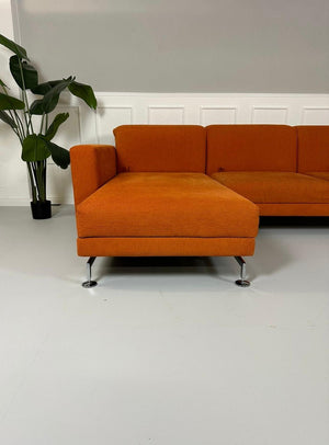 Gebrauchtes Brühl Moule Ecksofa Stoff in der Farbe Orange vor einer Wand, stilvoll und modern eingerichtet.