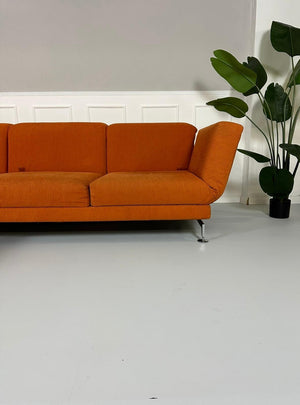 Gebrauchtes Brühl Moule Ecksofa Stoff in der Farbe Orange vor einer Wand, stilvoll und modern eingerichtet.