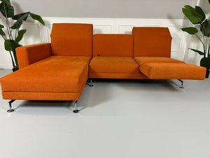 Gebrauchtes Brühl Moule Ecksofa Stoff in der Farbe Orange vor einer Wand, stilvoll und modern eingerichtet.