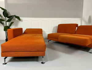 Gebrauchtes Brühl Moule Ecksofa Stoff in der Farbe Orange vor einer Wand, stilvoll und modern eingerichtet.